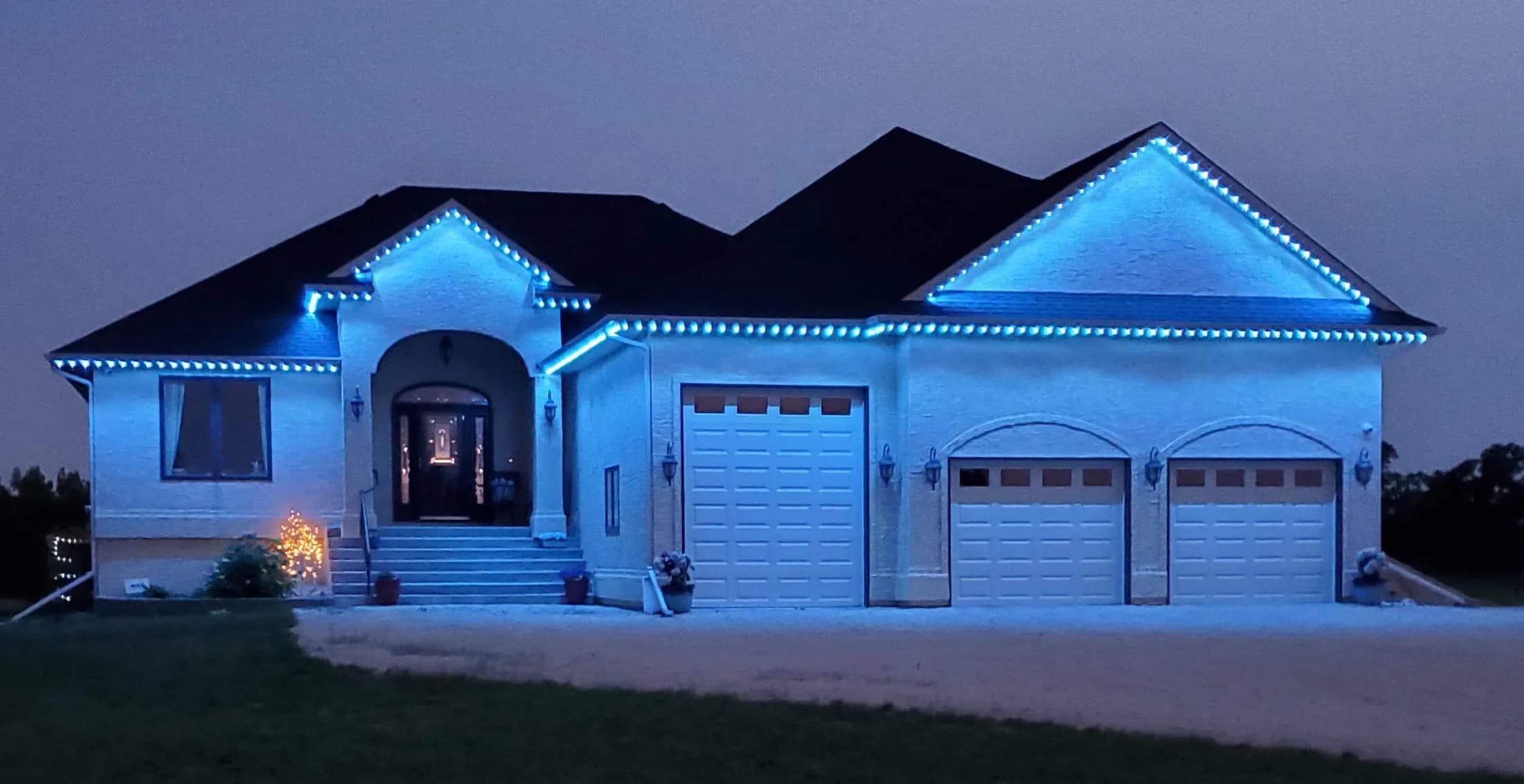 Wide home elevation lit in blue by app-controlled permanent LED track lighting