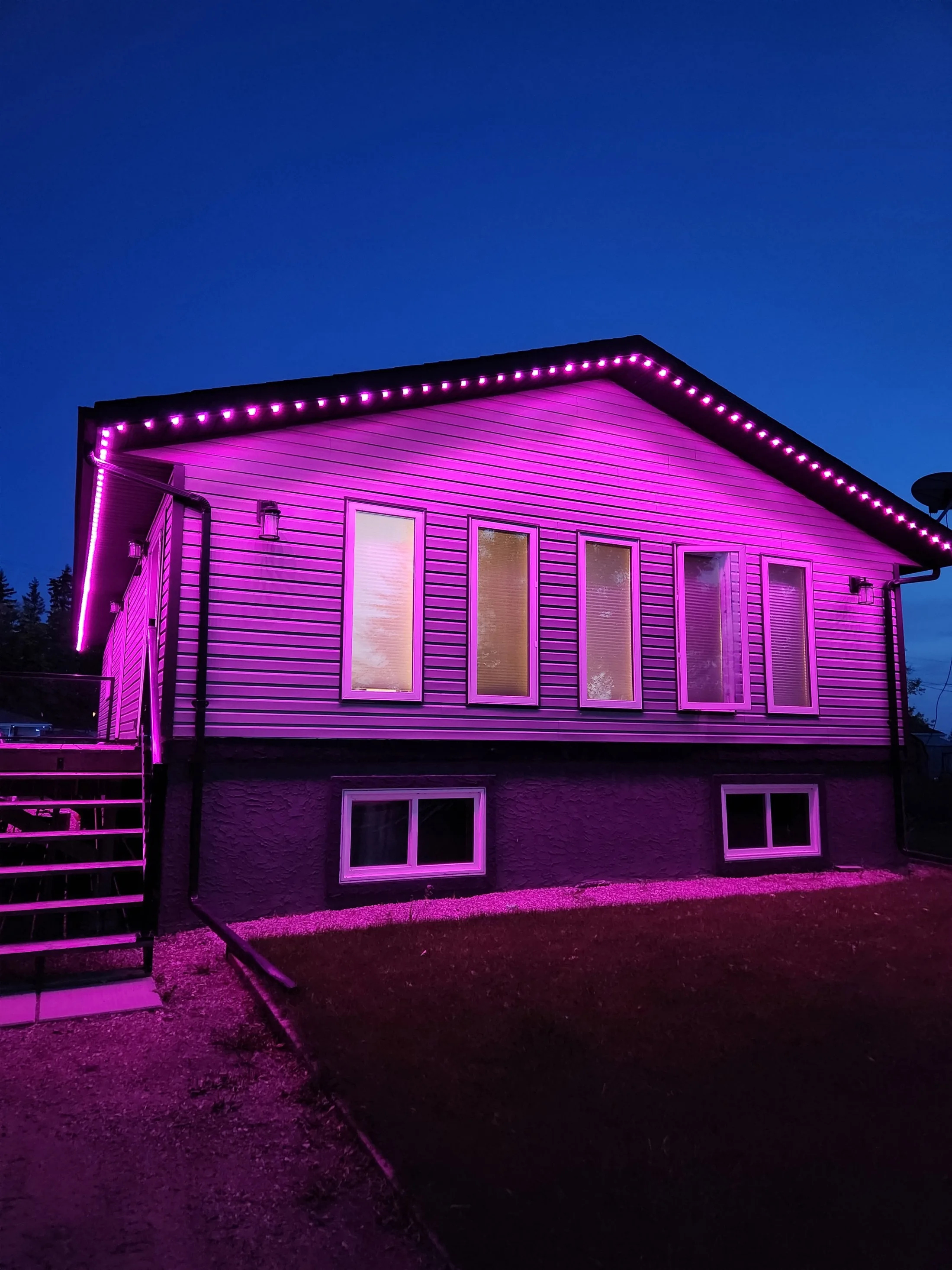 Track-mounted RGBW LED lights washing a house facade in pink and magenta