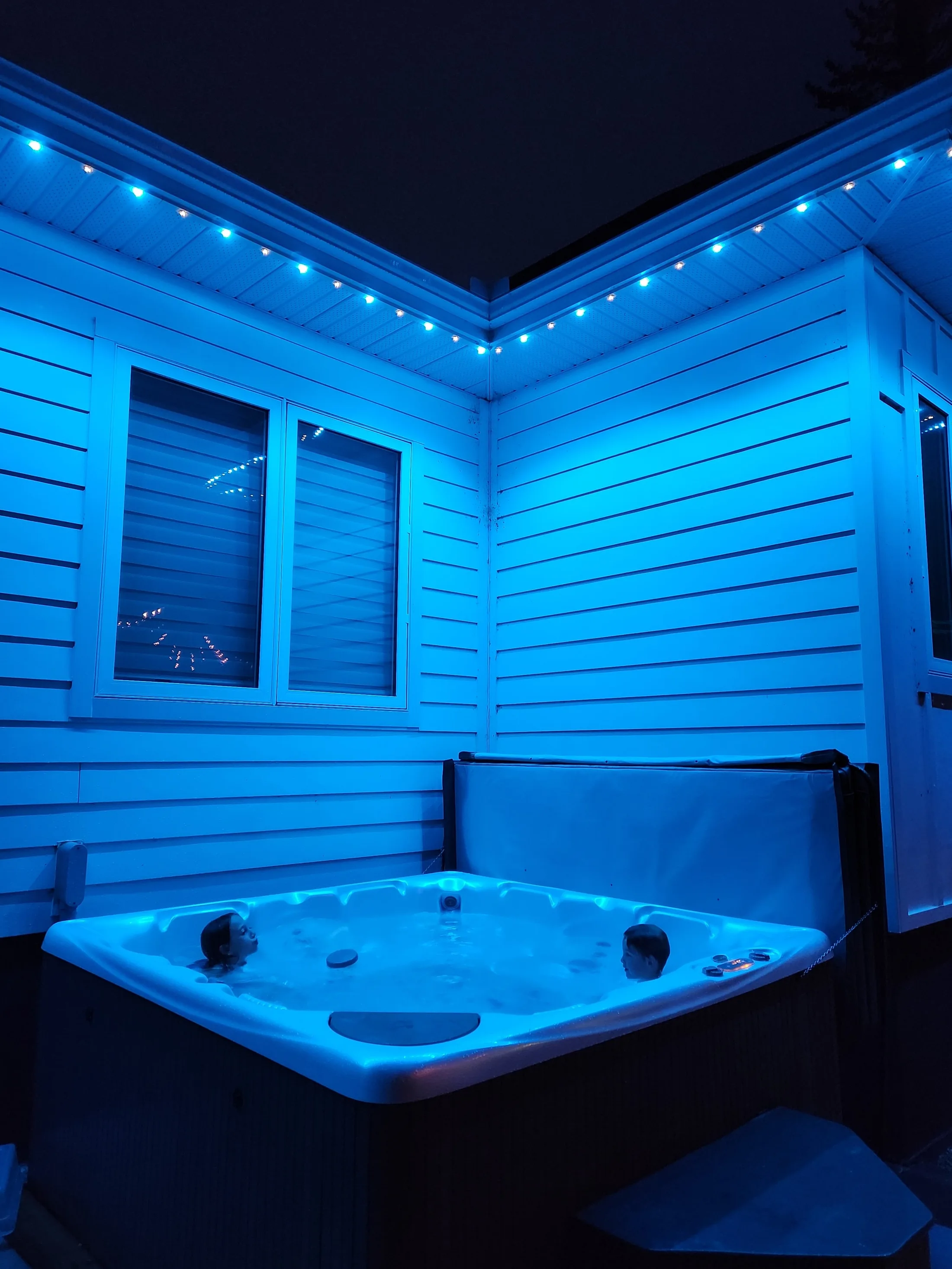 Backyard and hot tub area lit in teal by permanent LED lighting