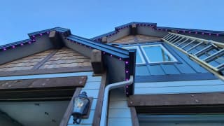 Permanent LED lights in purple along the rooflines of a craftsman-style home
