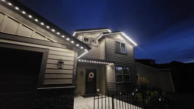 Warm white permanent LED roofline lights installed on a two-storey home at night