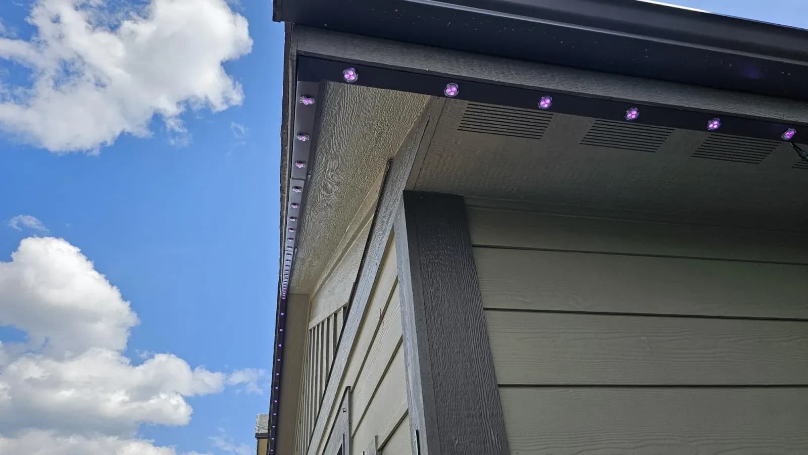 Close-up of the black aluminum permanent LED track and RGB puck lights mounted under a home's eave